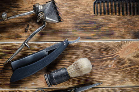 old hand hairdressing tools. Manual clipper, hairdressing scissors, straight razor, brush for shaving foam. on brown weathered wood background. top view flat layの写真素材