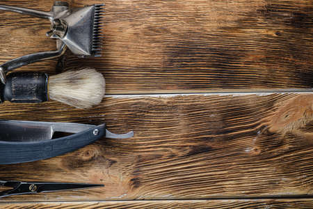 old hand hairdressing tools. Manual clipper, hairdressing scissors, straight razor, brush for shaving foam. on brown weathered wood background. top view flat layの写真素材