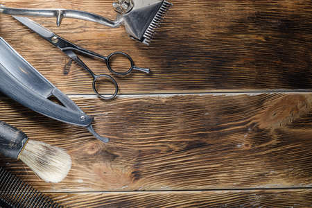 old hand hairdressing tools. Manual clipper, hairdressing scissors, straight razor, brush for shaving foam. on brown weathered wood background. top view flat layの写真素材