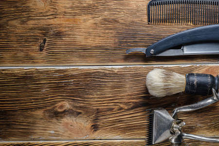 old hand hairdressing tools. Manual clipper, hairdressing scissors, straight razor, brush for shaving foam. on brown weathered wood background. top view flat layの写真素材