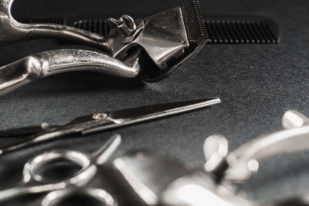On a black surface are old barber tools. Vintage manual hair clipper, comb, razor, hairdressing...