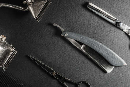 On a black surface are old barber tools. two vintage manual hair clipper, comb, razor, hairdressing scissors. black monochrome. Close-up. Barbershop background. contrast shadows. horizontalの写真素材