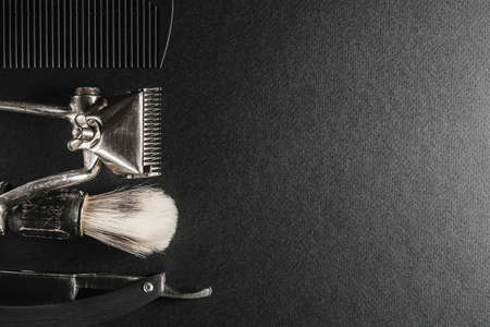 On a black surface are old barber tools.Two vintage manual hair clipper, comb, razor, shaving brush, hairdressing scissors. black monochrome. Close-up. Barbershop background. contrast shadows.の写真素材