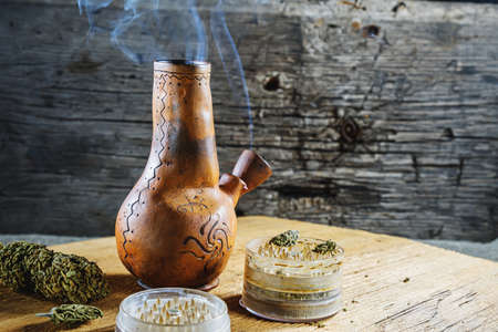 Old brown steamung bong and open cannabis grinder with chopped marijuana weed and medical cannabis...