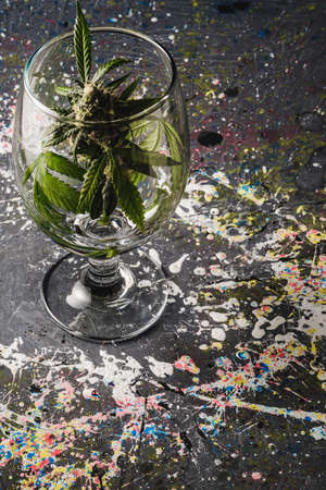 in the background in blur a bud of medical cannabis in a wine glass on a gray splashed paint background. Vertical orientationの写真素材