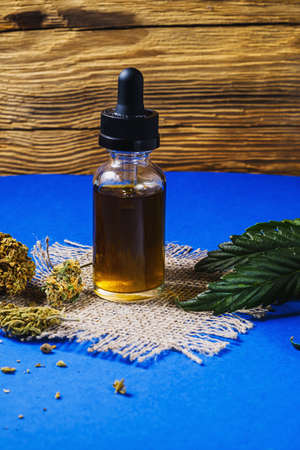 a vial with a dropper of cannabis concentrate cbd stands next to dried marijuana buds and a cannabis...