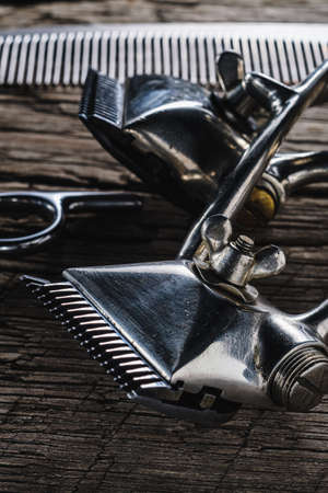 On a old wooden surface are old hairdresser tools. two vintage hand-held hair clipper and comb and seen hairdressing scissors. vertical orintationの写真素材