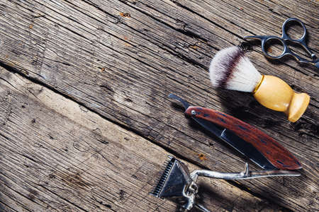 On a rustic wooden weathered surface are old barber tools. Vintage manual hair clipper comb razor shaving brush shaving brush hairdressing scissors. horizontal.の写真素材