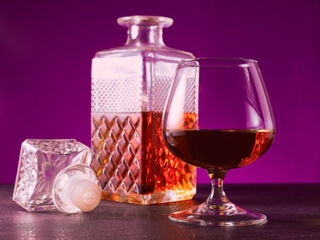 glass textured square bottle and glass goblet with amber alcohol brandy scotch whiskey. violet. Horizonalの写真素材
