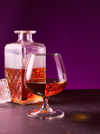 glass textured square bottle and glass goblet with amber alcohol brandy scotch whiskey. violet backgroundの写真素材