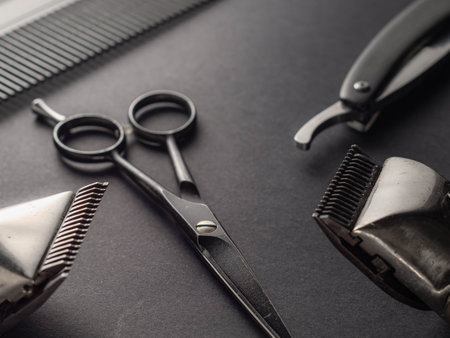 Various hair grooming tools are displayed on a dark surface. Scissors, clippers, and a comb highlight essential equipment for barbers or hairstylists working on haircuts.の写真素材