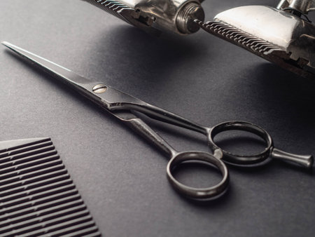 Scissors and styling tools are arranged neatly on a dark surface, reflecting typical equipment found in a barber shop or salon during a haircutting session.の写真素材