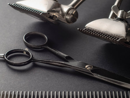 A collection of barber tools is displayed, featuring shiny clippers, sleek scissors, and a black comb resting on a dark surface. This setup emphasizes precision in grooming.の写真素材