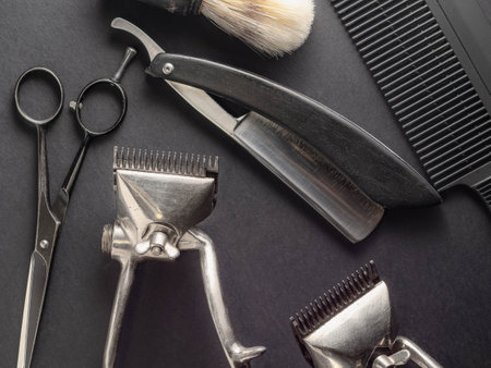 A collection of classic barber tools including scissors, clippers, a straight razor, and a shaving brush on a dark background. This arrangement highlights the artistry of traditional barbering.の写真素材