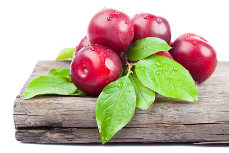 fresh plums with green leaves on wooden board の写真素材