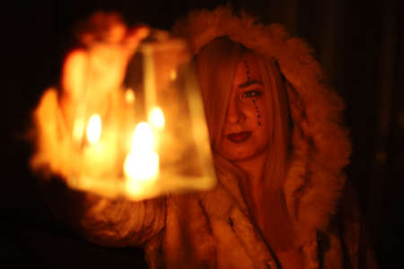 A woman in the form of a witch with symbols on her face and in a hood holds a vonar on her outstretched hand. Witch getting ready for halloween. Halloween celebration conceptの写真素材