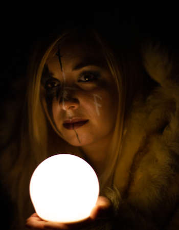 A woman in the Gothic image of a witch in the dark holds a luminous sphere in front of her on her...