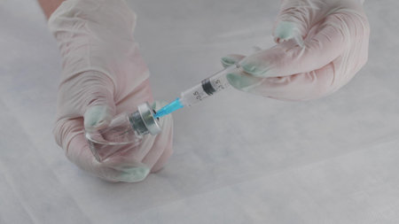 The doctor holds a glass bottle in his hands and draws medicine with a syringe with a needle. A doctor in white gloves prepares a syringe with medicine for injection. healthcare concept.の写真素材