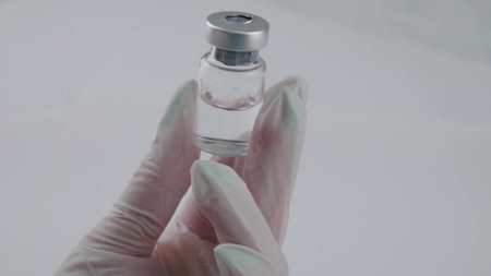 The doctor demonstrates a glass bottle with a transparent medicine holding it in his gloved hand....