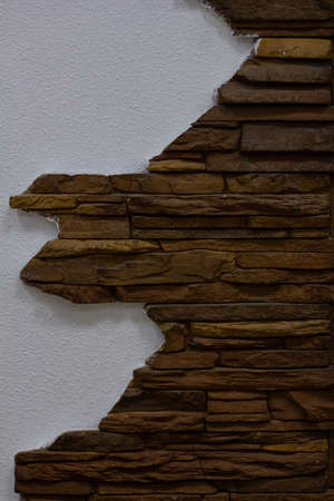 A close-up shot of a wall background with a beautiful texture lined with decorative brown stone beautifully intersecting with a white painted wall. Close-up of decorative stone texture. Decor concept.の写真素材