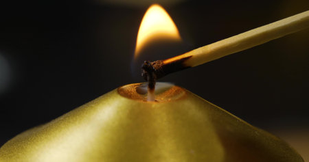 On a black background, a match lights the wick of a golden candle Beautiful close-up photo. Concept...