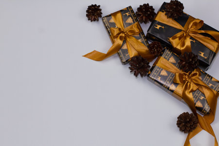 Christmas card with white background and space to insert words. In the corner are Christmas presents wrapped in black paper with a gold pattern and tied with a ribbon. Between them are pine cones.の写真素材