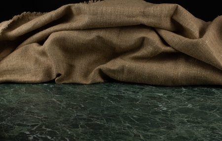 Calm background. On a green marble table lies a pile of beige linen or burlap. The beautiful texture of the fabric forms many folds. Shot close-up, visible threads and texture of the fabric.の写真素材