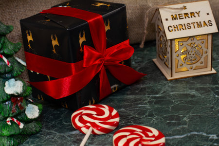 Christmas decoration. A gift with a red bow, peppermint lollipops, a toy house lie on the table against the background of linen fabric. Idea for decorating your home for Christmas.の写真素材