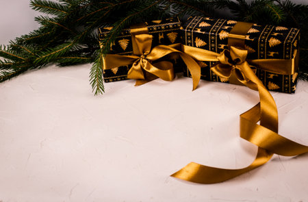 In preparation for Christmas, two Christmas gifts with a beautiful golden ribbon and bows lie on a white background. Fir branches are visible in the background. Christmas card concept.の写真素材