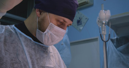 Against the background of the surgeons cute face, you can see a clamp with a needle and thread. Handsome higugr man finishes the operation and performs wound closure. Close-up concept.の写真素材