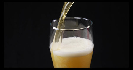 Beer with lush foam in a glass on a black background. Yellow beer is poured from a bottle into a glass, which rises with lush white foam. The concept of beer with foam.の写真素材