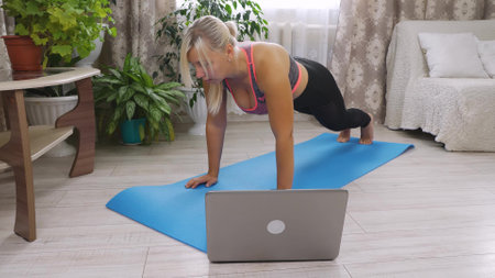 A blond woman is exercising in a bright room to lose weight. A slightly overweight woman exercising on a gym mat in the living room during the day. The concept of a healthy lifestyle.の写真素材