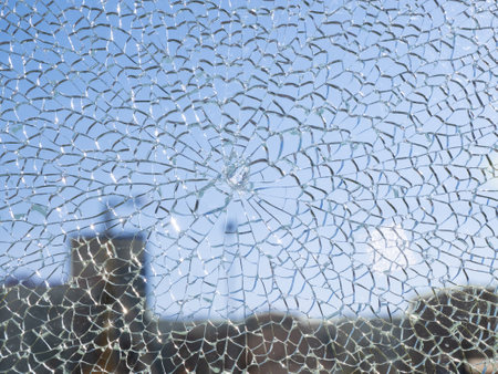 The blue sky is visible through broken glass. The glass has cracked into many cracks and creates a beautiful cellular structure. Broken glass concept.の写真素材
