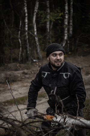A man with a beard pulls a tree trunk with branches from a pile of fallen trees. A man in work clothes sorts a blockage of trees. The concept of a strong man.の写真素材