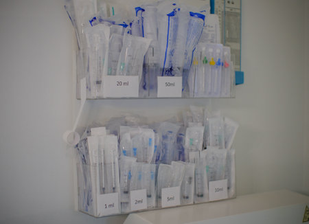Boxes with packaged syringes and intravenous catheters hang on a white wall. Sterile packed syringes and catheters are laid out in the doctors treatment room.の写真素材