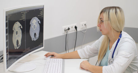 A serious doctor sits at a computer and closely examines the mri examination of a pet with a head injury. The skeleton of the pets head is visible on the computer monitor against a black background.の写真素材