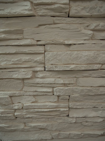 The wall is lined with white artificial stone. When close-up, the texture of the stone, its irregularities and edges are clearly visible. Background of artificial stone for wall decoration.の写真素材