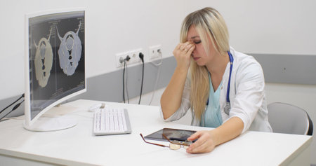 Late in the evening the veterinarian was very tired from a lot of work. The doctor sits at the table taking off his glasses and rubs the bridge of his nose trying to relieve tension from his eyes.の写真素材