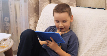 The boy draws enthusiastically on the tablet. The boy thought about the drawing and holds a pen in...