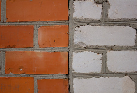 Background of a brick wall where half is lined with red brick and half is white. A brick of rare stones divides the wall into two halves. Combinations of two colors of bricks in the background.の写真素材