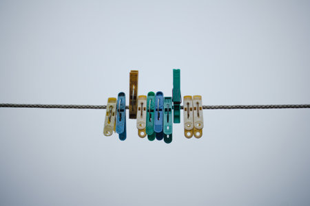 Clothespins hang in a row on a stretched rope against a cloudy sky. Rope for drying clothes on the street with multi-colored clothespins. Plastic old clothespins.の写真素材