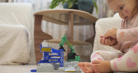 A beautiful little girl with a scratch on her cheek carefully plays with toys. The cute little girl loves to play with her brothers toys. The child is fascinated by looking at a new toy.の写真素材