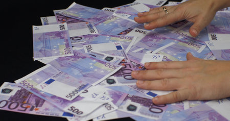 Hands raking a big pile of money er bills from a black background. Womens hands lie on top of a large pile of five hundred euro bills. The concept of a big win euro bills.の写真素材