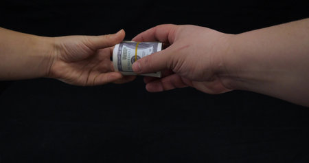 Two hands hold one hundred dollar bills on a black background. Transfer stacks of money dollars on a black background. One hundred dollar bills rolled into a tube.の写真素材