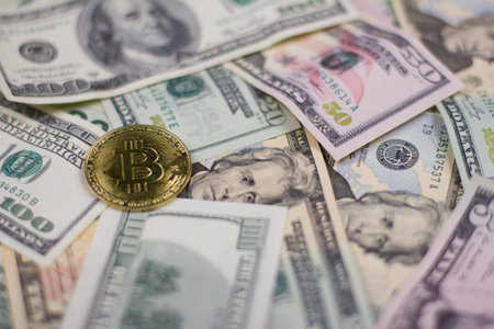 Against the background of many dollar bills lies a gold coin bitcoin. Close-up. Dollars of wound value lie under the crumpled bitcoin sign. Concept background from dollars and bitcoin coins.の写真素材