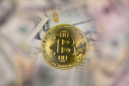 Bitcoin coin magnified under a magnifying glass against the background of dollar bills. Background from dollars with bitcoin in the center and a magnifying glass.の写真素材