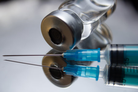 An opened medicine bottle on a mirror with an open syringe. After the injection, the used syringe lies on a mirror surface with an open vial. The concept of a used syringe and a medicine bottle.の写真素材