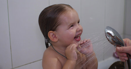 The child laughs sweetly and smiles at his mother who washes him. Girl child smiles broadly standing...