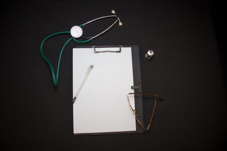On a black background lies a medical tablet, stethoscope, pen, glasses. Background with medical attributes. Examination by a cardiologist with a stethoscope.の写真素材