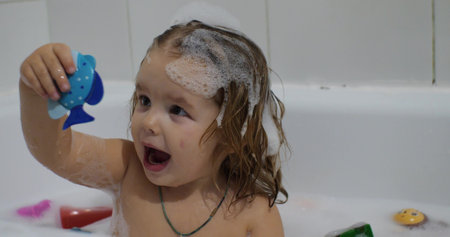The childish emotions on the face of a girl bathing in a bath with foam are exalted. The little girl...